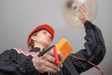 Electrician technician measures the voltage in the lamp socket of a residential electrical system and changes the light bulb. female electrician using a multimeter