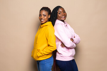 Portrait of two cheerful young women standing together isolated over beige background