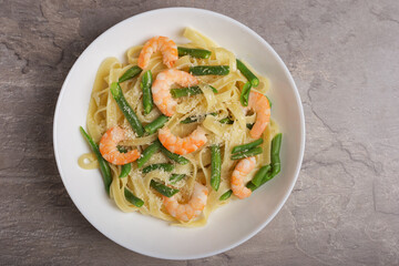 Top view on a plate of Tagliatelle with shrimps and green beans with grated Parmesan cheese on dark stone table. Italian pasta. Mediterranean cuisine.