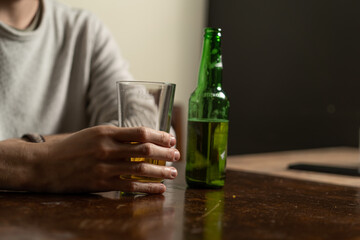 Guy holding a glass of beer sitting in a pub. Close up of the hand near the green bottle. Alcohol...