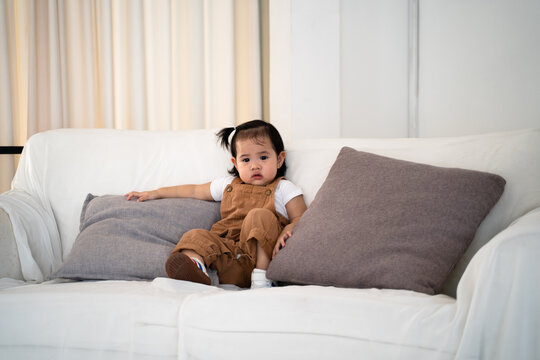 portrait of asian baby infant in brown standing in white artis drawing room near sofa couch.