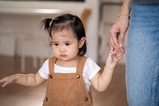 portrait of asian baby infant in brown holding mother hand walking at home. toddler secured with mom. kid confident when support.