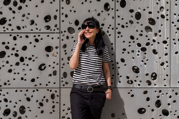 Adult woman wearing sunglasses talking on the phone on the street on a sunny day.