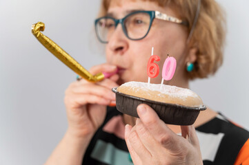 Happy caucasian woman celebrating 60 years birthday and blowing a whistle in tongue on white background.