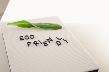 Zero waste concept, pros and cons. Black letters on a peg board with message text Eco friendly and a fresh green leaf on white background. Flat lay.