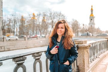 Fototapeta premium A young woman stands on the embankment of Saint Petersburg with a view of old buildings, early spring