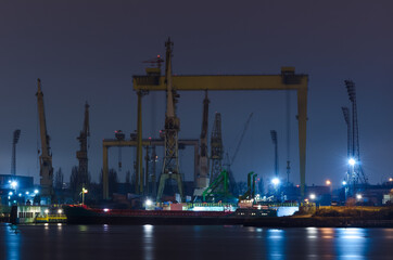 Obraz premium SHIPYARD AT NIGHT - Ship at the quay and a slipway with cranes 