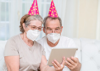 Senior couple wearing party's caps and protective masks celebrates  birthday with her family on...