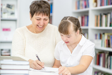 Fototapeta na wymiar Smiling teacher and girl with syndrome doing homework together. Education for disabled children concept