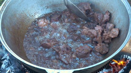 The meat is boiling in a large cauldron for pilaf. Campfire cooking.
