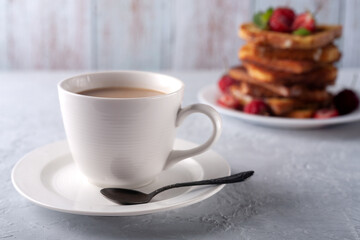 A cup of coffee with cream and French toast with cinnamon and strawberries. Morning breakfast