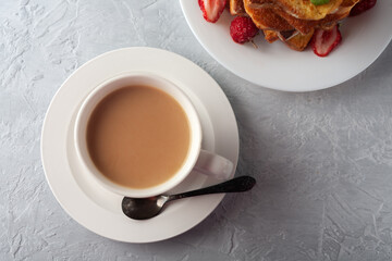 A cup of coffee with cream and French toast with cinnamon and strawberries. Morning breakfast