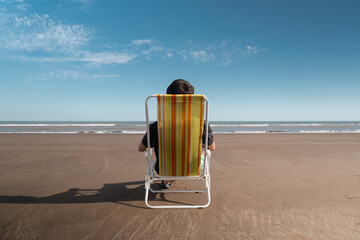 Young man on vacation at the beach enjoying sitting on the deck chair. Back view.