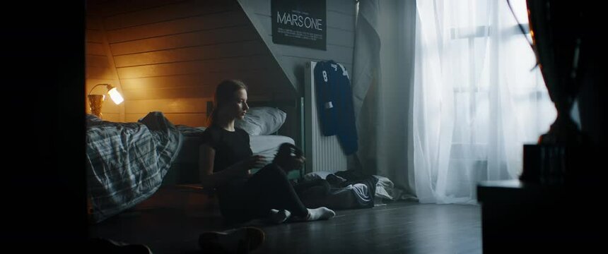 WIDE Attractive Caucasian teenager girl putting on baseball glove in her attic bedroom at home. Shot with 2x anamorphic lens