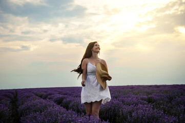 Fototapeta na wymiar Portrait of a young woman in white dress and straw hat walking in the lavender field