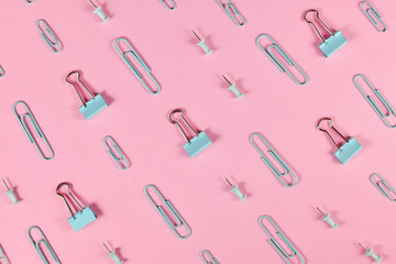 Stationery items like paper clips and drawing pins arranged on pink background 