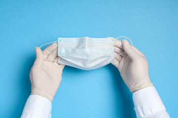 hands in medical gloves with a medical breathing mask on a blue background, health care prevention of coronavirus infection, as well as other viruses and pollution