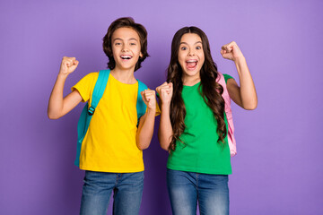 Photo of two school kids happy positive smile celebrate win victory fists hands hold rucksack isolated over violet color background