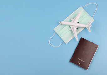 flat lay of airplane model on  medical face mask and passport  on blue background. Traveling during covid-19 epidemic concept.