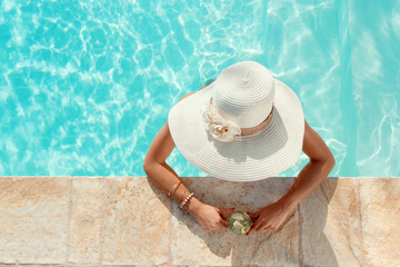 Young woman in a straw hat with tropical cocktail in a pool