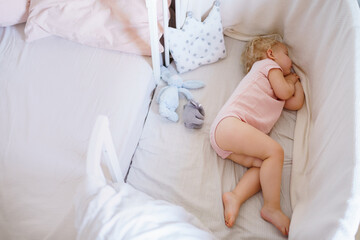 A small child in pink pajamas sleeps in his crib at home. Healthy daytime sleep.