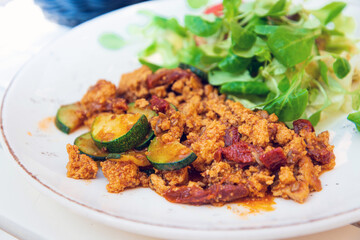 Vegan breakfast prepared with scrambled tofu and eggs, cooked with dried tomatoes and zucchini served with fresh lettuce and cucumber in white ceramic vintage plate