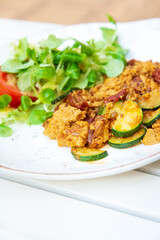 Vegan breakfast prepared with scrambled tofu and eggs, cooked with dried tomatoes and zucchini served with fresh lettuce and cucumber in white ceramic vintage plate