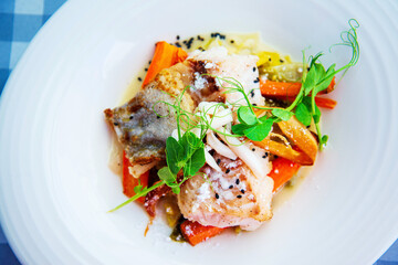 Delicious fillet of cod fish with carrots, leeks and mushrooms in white plate ready to be served