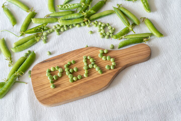 Fresh green peas decoration with PEAS word made of green peas on a wooden tray, top view