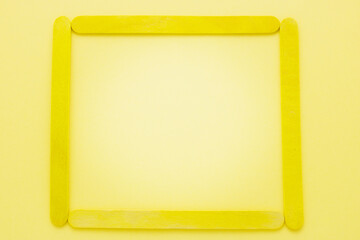 Yellow popsicle stick make to square frame with space inside on yellow paper background. Beautiful yellow background.