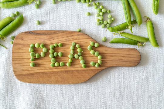 Fresh green peas decoration with PEAS word made of green peas on a wooden tray, top view