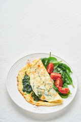 Omelet or omelette with spinach, cherry tomato and pepper seasoning on a white plate, on white background. Top view.