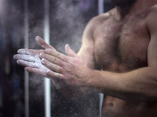 Hands of a muscular athlete in talcum powder on a dark background