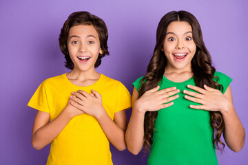 Photo of brown haired amazed little boy and girl ask me wear green yellow t-shirt isolated on...