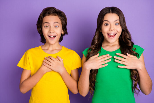 Photo of brown haired amazed little boy and girl ask me wear green yellow t-shirt isolated on purple color background