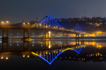 Pedestrian bridge in Kiev. Evening lighting. Reflection of the bridge in the river.