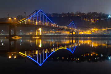 Pedestrian bridge in Kiev. Evening lighting. Reflection of the bridge in the river.