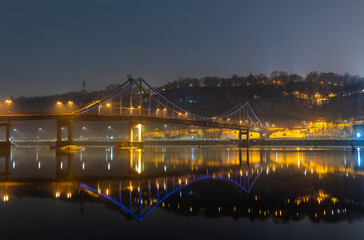 Pedestrian bridge in Kiev. Evening lighting. Reflection of the bridge in the river.