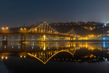 Pedestrian bridge in Kiev. Evening lighting. Reflection of the bridge in the river.