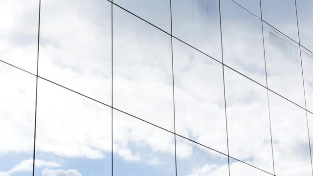 Skyscraper office building glass square windows blue cloudy sky reflection modern abstract corportate background texture, gentle movement, closeup, long clip. Sky reflecting in the windows, angle