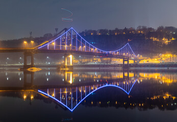 Pedestrian bridge in Kiev. Evening lighting. Reflection of the bridge in the river.