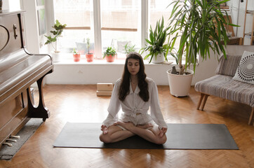 One beautiful young woman is doing yoga on an exercise mat in her living room. The room and her...