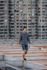 Man walking on the rooftop, wearing casual, curly hair collected in the pony tail. Background of residential building. Urban rooftopper extreme lifestyle, cityscape, abandoned atmosphere