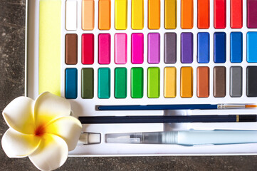 A palette of bright multicolored watercolors, brush and pencil close-up, artist's tools all colors...