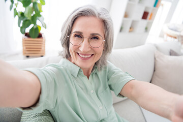 Portrait of cheerful woman sit on sofa make selfie toothy smile enjoy spend free time vacation home indoors