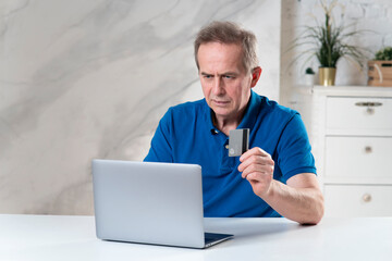 Portrait of handsome senior elderly retired man with laptop computer holding credit bank card, paying ordering in online internet store, shop at home, doing secure payment. Online shopping concept