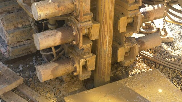 CLOSE UP: Massive drill spins and drills into the soil at a construction site in the sunny countryside. Heavy industrial rig bores a hole in the ground during modern geothermal pump installation.