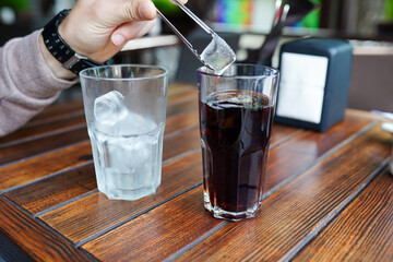 A glass of fresh ice cold lemonade on wooden table of coffee . Close up of male hand, man holding ice