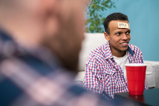 A group of friends are hanging out in the living room. A black american student boy plays who i am with his college friends with Sticky Papers Attached to Foreheads - Powered by Adobe