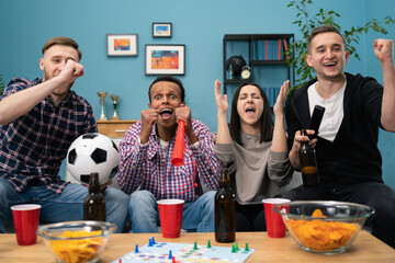 Happy diverse group of student sports fans throwing arms up in excitement celebrating goal watching sports event on TV together bonding as friends eating snacks drinking beer